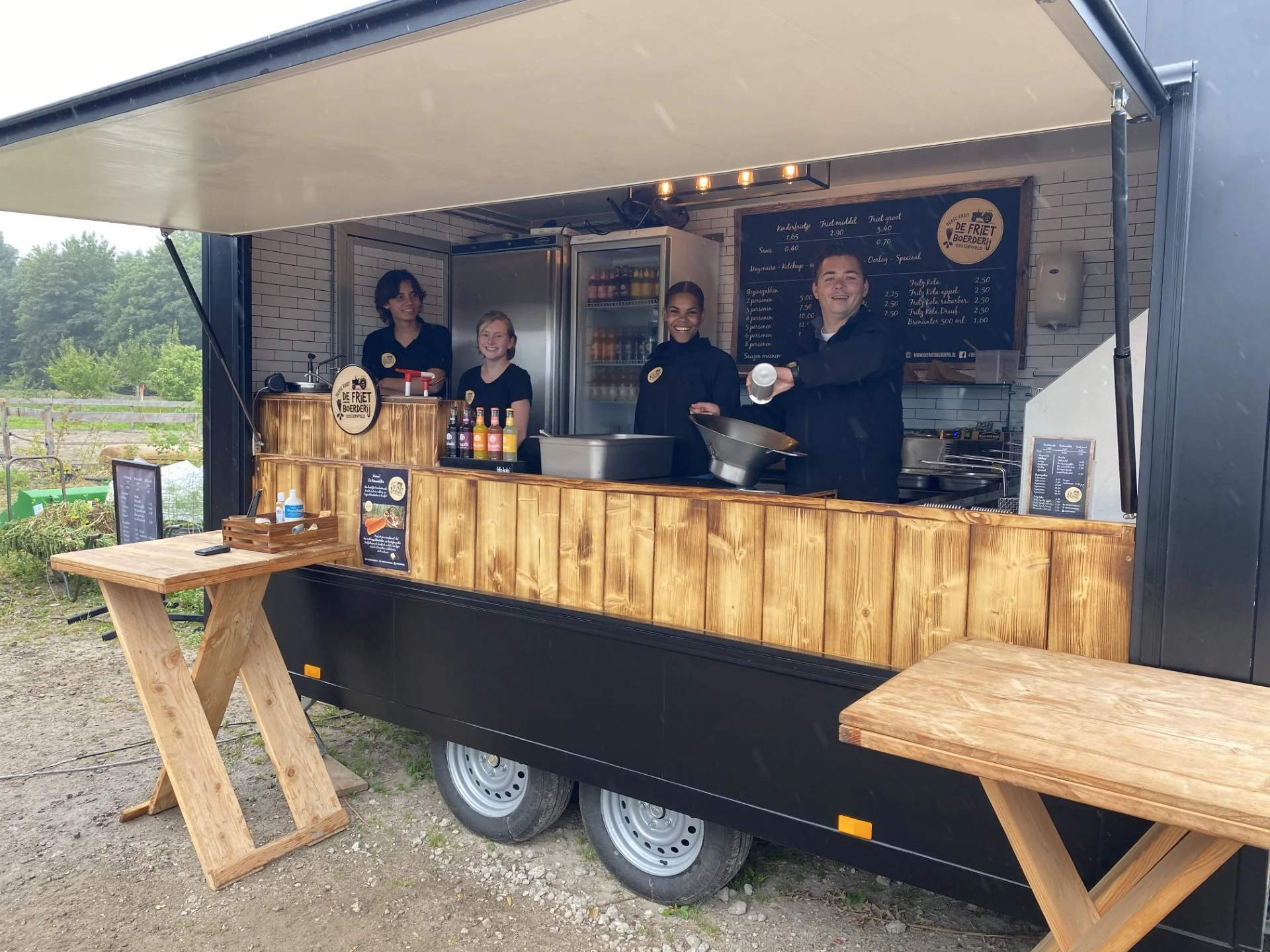 Team van De Frietboerderij Events bij de geopende kraam met menubord en houten picknickbankjes op locatie